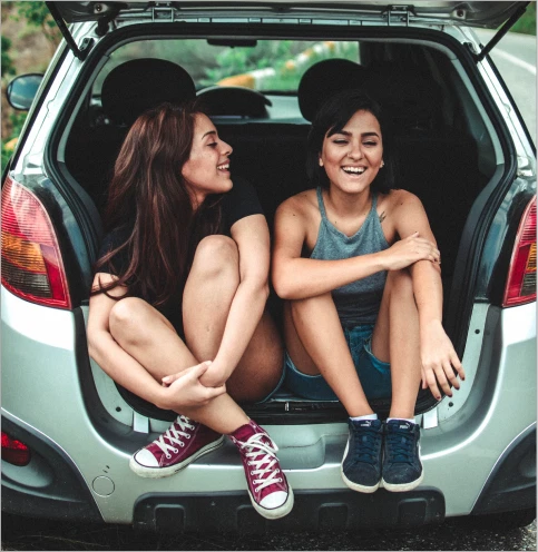 Two women sitting in the open boot of a car, smiling